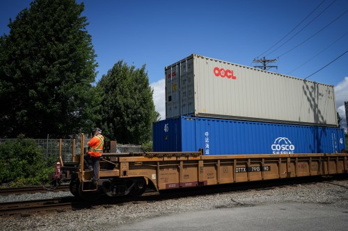 A worker rides on the outside of a rail well car as a CN Rail train moves containers from port, in Vancouver, on Wednesday, June 10, 2026. THE CANADIAN PRESS/Darryl Dyck