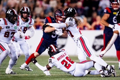 Montreal Alouettes' Travis Theis (5) is tackled by Ottawa Redblacks' King Ambers (27) and Shadwel Nkuba II (28) during CFL action in Montreal on Aug. 20, 2026. THE CANADIAN PRESS/Christopher Katsarov