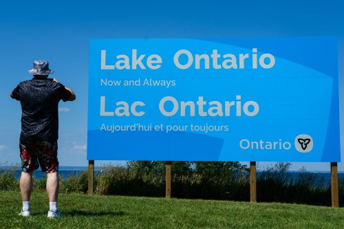 A person takes a picture of the newly unveiled sign for Lake Ontario at Fifty Point Conservation Area in Grimsby, Ont., on Saturday, Aug. 29, 2026. THE CANADIAN PRESS/Keito Newman