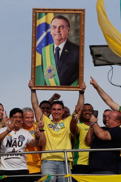 Opposition presidential candidate Flavio Bolsonaro holds a photo of his father, former President Jair Bolsonaro, as he rides a boat during a campaign rally ahead of the October general election in Angra dos Reis, Rio de Janeiro state, Brazil, Saturday, Aug. 29, 2026. (AP Photo/Bruna Prado)