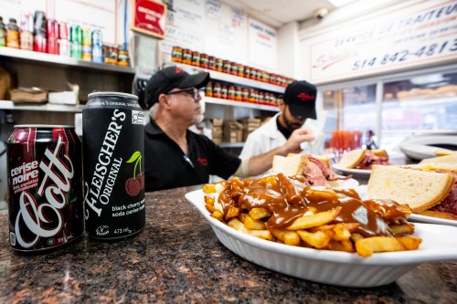 Smoked meat sandwiches and poutine wait to be served next to a can of Canadian made Fleischer's black cherry soda, which replaced the long used Cott's black cherry soda at Schwartz's deli, in Montreal on Tuesday, Aug. 25, 2026. THE CANADIAN PRESS/Christopher Katsarov