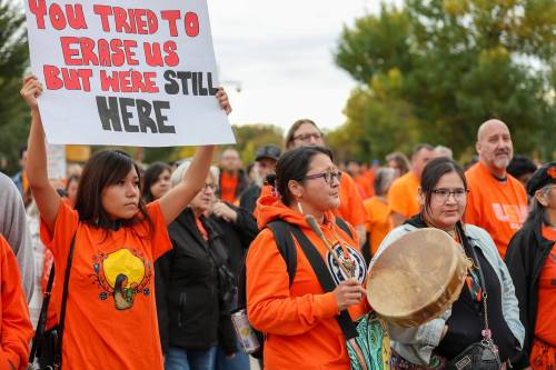 Torri Hirsch McKay holds a sign while she participates in the Orange Shirt Day Healing Walk, while Monica Campeau plays an Indigenous hand drum. (Brook Jones / Free Press)