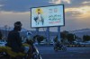 People ride their motorbikes under a billboard showing Houthi leader Abdul Malik al-Houthi with a phrase that reads in Arabic; 