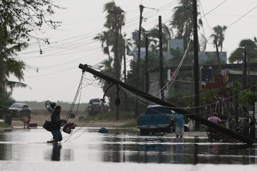 A man carries items through floodwater past downed electric lines after the passing of Hurricane Polo in Puerto San Carlos, Baja California Sur state, Mexico, Tuesday, Sept. 29, 2026. (AP Photo/Eduardo Verdugo)
