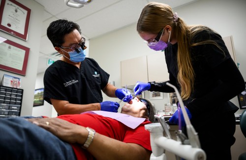 Dr. Melvin Lee, left, performs a tooth extraction for patient Robert McFarlane, who is eligible for the Canadian Dental Care Plan, as team member Sofia Christow-Filleul assists at his dental clinic in Ottawa, on Wednesday, Aug. 7, 2024. THE CANADIAN PRESS/Justin Tang