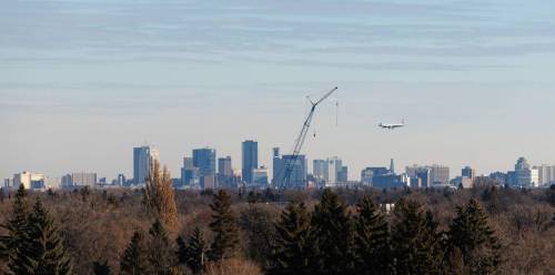 MIKE DEAL / WINNIPEG FREE PRESS An Air Canada plane heads in for a landing about to fly past a crane which is set up at 215 Sinawik Bay where construction of a new building that will open in 2024 as part of the St. James Kiwanis Village, a seniors housing project, with the Winnipeg skyline in the distance Wednesday morning. 231129 - Wednesday, November 29, 2023.