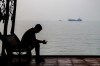A man checks his cellphone at a waterfront shelter as commercial vessels appear anchored in the Strait of Hormuz off Bandar Abbas, Iran, Monday, Tuesday, Oct, 6, 2026. (Amirhosein Khorgooi/ISNA via AP)