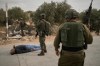 Israeli soldiers stand beside a wounded Palestinian man lying on a road after soldiers shot him following a settler attack on Palestinians harvesting olives in the occupied West Bank village of Abu Falah, Friday, Oct. 16, 2026. (AP Photo/Leo Correa)