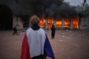 A protester wraps a French flag around them in front of the burning tourism office during a demonstration against rising living costs and in solidarity with students’ grievances in Lyon, France, Saturday, Oct. 17, 2026. (AP Photo/Laurent Cipriani)