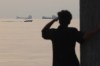 A man looks out over the water as a small boat passes cargo ships anchored in the Strait of Hormuz off Bandar Abbas, Iran, early Saturday, Oct. 24, 2026. (Amirhosein Khorgooi/ISNA via AP)